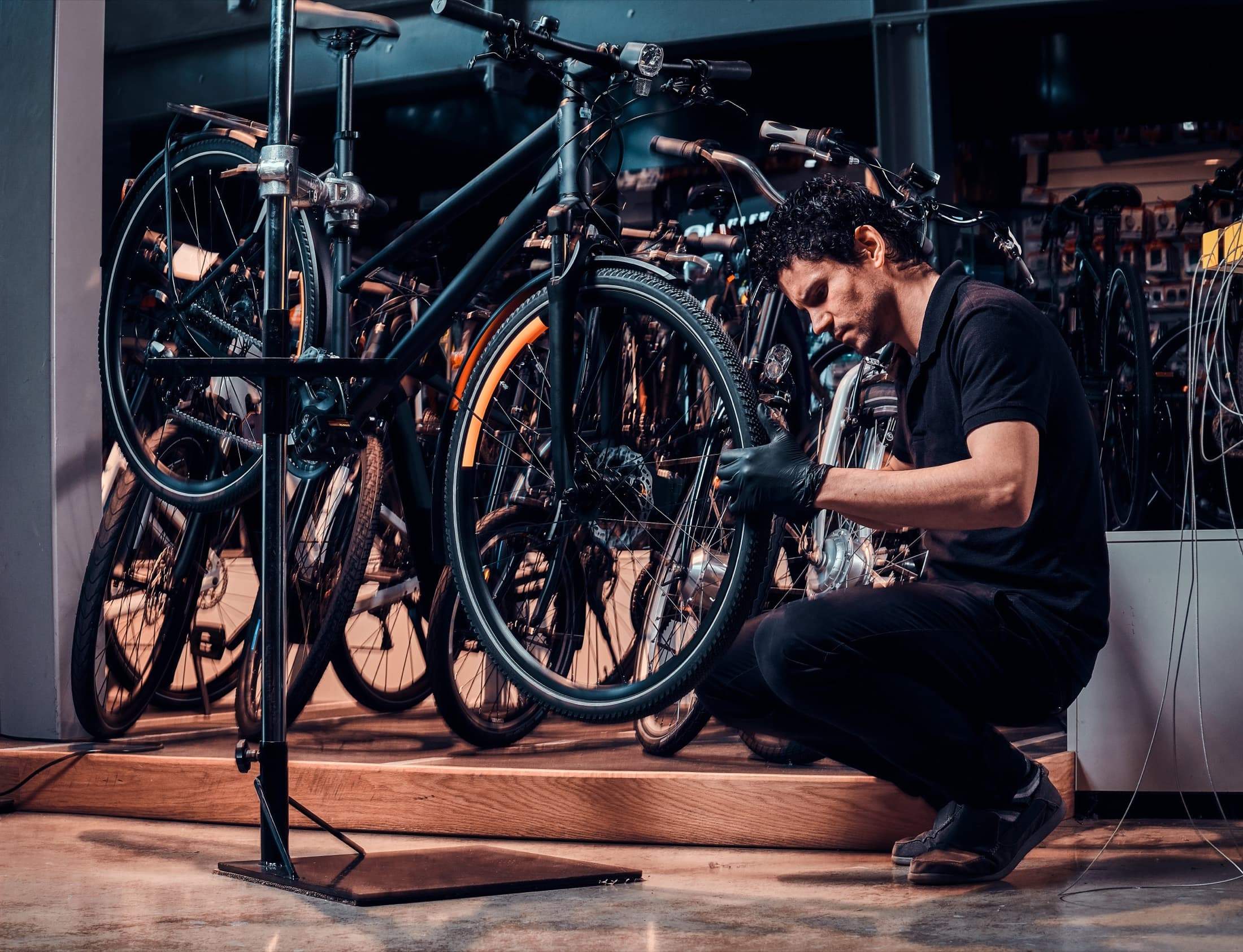 A mechanic at the repair stand, working on a bike held in a workshop clamp.